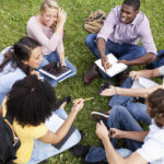 Group of teenagers studying and laughing on the grass