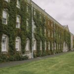 Image of an old time university building sitting on grass. Building has ivy all over it.
